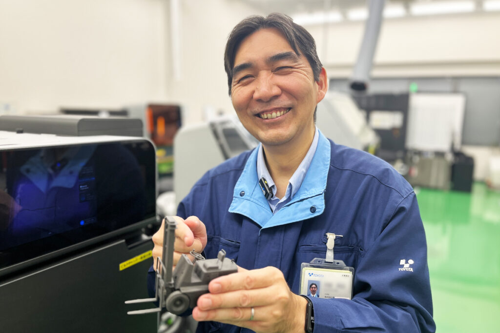 造形につかったFuseの前で初代フォークリフトを見せてくれた大岩氏。サポートレスでレバーのような細部まで精密に造形できる点が社内に評価されているという。